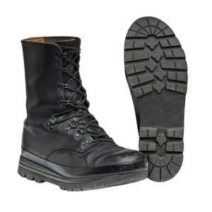 Puede incluir: Bota de combate de cuero negro con suela gruesa y cierre de cordones. La bota presenta un diseño de caña alta y un patrón de banda de rodadura resistente en la suela. La imagen también muestra la suela de la bota.
