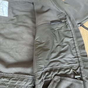 May include: A dark green fleece jacket with a zipper closure and multiple pockets. The jacket has a fleece lining and a drawstring at the waist.