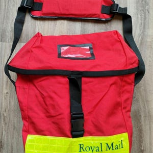 Może przedstawiać: Czerwona torba kurierska z czarnym paskiem i żółtym odblaskowym paskiem. Torba ma przezroczyste okienko i zielony napis "Royal Mail".
