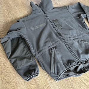 May include: A black fleece jacket with a zipper closure and multiple pockets. The jacket has a high collar and a ribbed cuff on the sleeves.