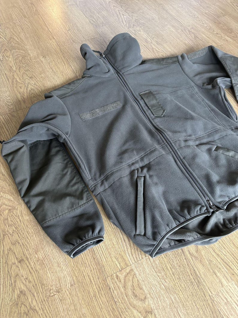 May include: A black fleece jacket with a zipper closure and multiple pockets. The jacket has a high collar and a ribbed cuff on the sleeves.