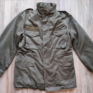 Peut inclure: Veste de style militaire vert olive avec plusieurs poches et un col montant. La veste a une fermeture à boutons et un écusson sur la manche. Fabriquée dans un matériau durable, elle est adaptée aux activités en extérieur.