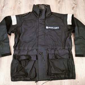 May include: A black jacket with a white reflective strip on each sleeve and a patch that says "ROYAL NAVY" on the chest.