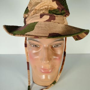 May include: A camouflage bucket hat with a brown, green, and tan pattern. The hat has a wide brim and a chin strap.