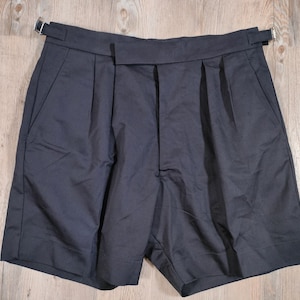 May include: Black pleated shorts with a belt loop and buckle closure.