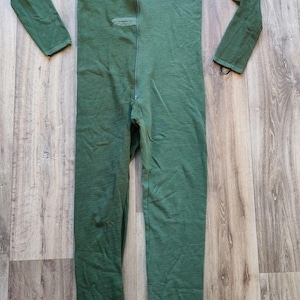 Puede incluir: Mono de una pieza verde oscuro con mangas y perneras largas. Cuenta con cremallera completa y estribos en los tobillos. La tela parece ser de punto suave. Prenda cómoda.