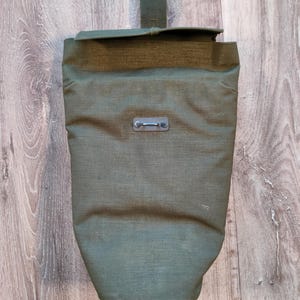 Peut inclure: Un sac en toile vert avec un rabat supérieur et une fermeture à boucle métallique. Le sac a une sangle avec une boucle métallique.