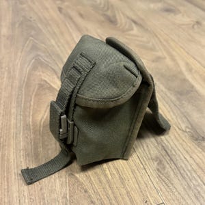 May include: A green canvas camera bag with a strap and a buckle closure.