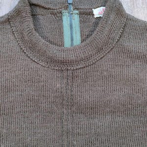 Puede incluir: Un su&eacute;ter de punto marr&oacute;n con una cremallera en la espalda. El su&eacute;ter tiene un cuello alto y una textura acanalada.