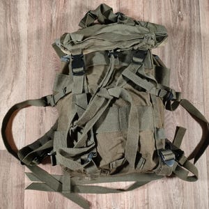 May include: A green canvas backpack with multiple straps and buckles. The backpack has a flap with a zipper closure.