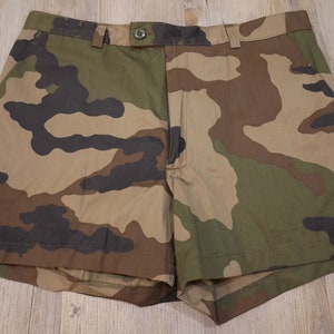 Puede incluir: Pantalones cortos de estampado de camuflaje en tonos marrones, verdes y negros. Los pantalones cortos tienen cierre de botón y cremallera.