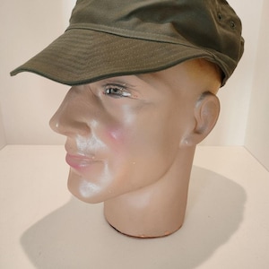 Peut inclure: Une casquette de style militaire verte avec une visière courte et un bouton sur le dessus.