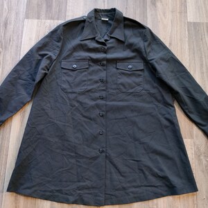May include: A dark grey long-sleeved shirt with a button-down front and two flap pockets. The shirt has a relaxed fit and a slightly A-line shape.