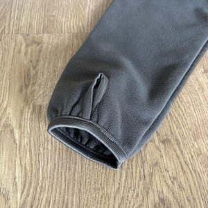 May include: Close-up of the dark green fleece cuff of a jacket with a sewn-in elastic band.