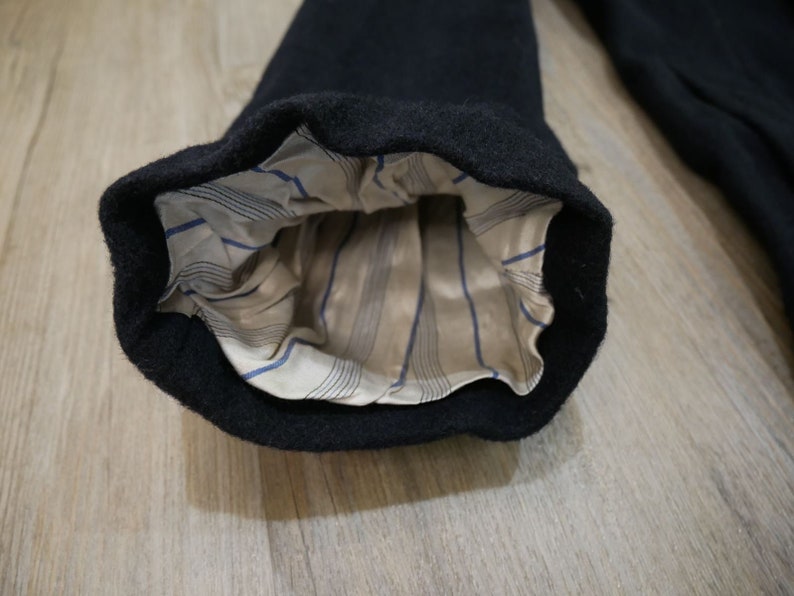 May include: Close-up of the inside of a black wool coat sleeve. The sleeve is lined with a beige fabric with thin blue stripes.