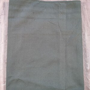 Puede incluir: Una toalla de cocina de tejido de waffle verde oscuro. La toalla está doblada por la mitad y colocada plana sobre una superficie de madera.