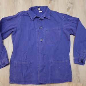 Peut inclure: Veste de travail vintage bleu indigo avec col, trois boutons et deux poches avant. La veste à manches longues a des poignets boutonnés et une petite poche poitrine. Le tissu présente un tissage en chevrons subtil.