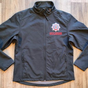 Può includere: Giacca grigio scuro con zip e collo alto. La giacca presenta un logo sul petto con la scritta rossa "NORTH YORKSHIRE FIRE AND RESCUE SERVICE". Ha due tasche con zip e una zip a tutta lunghezza.