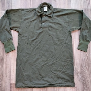 Könnte beinhalten: Ein langärmliges, olivgrünes Poloshirt mit Knopfleiste und einem einzigen Knopfverschluss.