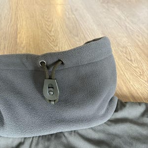 May include: A gray fleece jacket with a drawstring hood and a black toggle. The jacket has a zipper closure and a soft, comfortable feel.