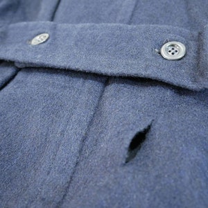 May include: A close-up of a dark blue wool jacket with a small tear in the fabric. The jacket has a button closure and a single button on the front.