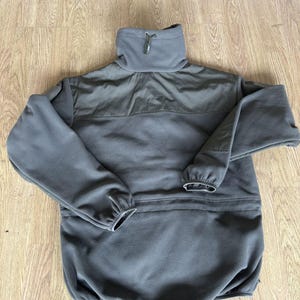 May include: A dark gray fleece jacket with a high collar and a zipper closure. The jacket has a pocket on the front and a drawstring at the waist.
