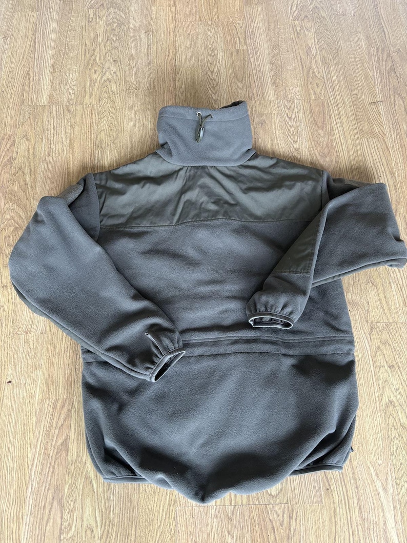 May include: A dark gray fleece jacket with a high collar and a zipper closure. The jacket has a pocket on the front and a drawstring at the waist.