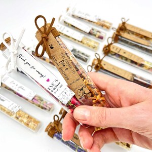 May include: A collection of small glass tubes filled with dried flowers and herbs, tied with twine and a small tag. The tags have handwritten text that says "Welcome to Eve's Bridal Shower" and "Thank you for coming!"