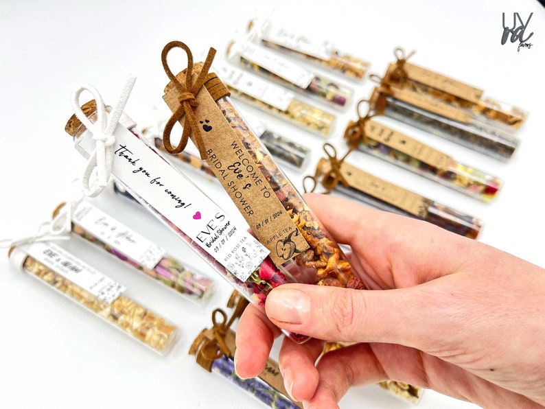 May include: A collection of small glass tubes filled with dried flowers and herbs, tied with twine and a small tag. The tags have handwritten text that says "Welcome to Eve's Bridal Shower" and "Thank you for coming!"
