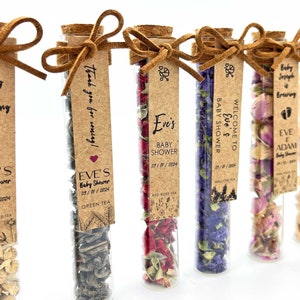 May include: Six glass test tubes filled with different types of dried flowers and herbs, each with a brown paper tag tied around the top with a brown suede ribbon. The tags have text that says "A Baby is Brewing", "Thank you for coming!", "Eve's Baby Shower", "Welcome to Eve's Baby Shower", "Baby Joseph is Brewing", and "Eve & Adam Baby Shower".