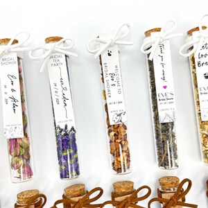 May include: Assortment of small glass test tubes filled with dried tea leaves and flowers. Each tube has a white label with black text, including the words "Bridal Shower", "Eve & Adam", "Welcome to Eve's Bridal Shower", "Let Love Brew", and "Thank you for coming!"
