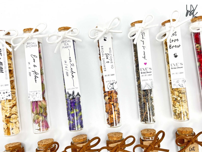 May include: Assortment of small glass test tubes filled with dried tea leaves and flowers. Each tube has a white label with black text, including the words "Bridal Shower", "Eve & Adam", "Welcome to Eve's Bridal Shower", "Let Love Brew", and "Thank you for coming!"