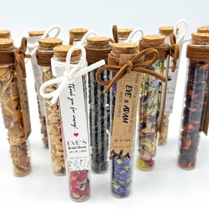 May include: A collection of small glass tubes filled with dried flowers, herbs, and fruit. Each tube is tied with a brown ribbon and a small tag with the text "Thank you for celebrating with us Eve & Adam Bridal Shower" and "Thank you for coming! Eve's Bridal Shower 05/11/2024 Red Rose Tea".