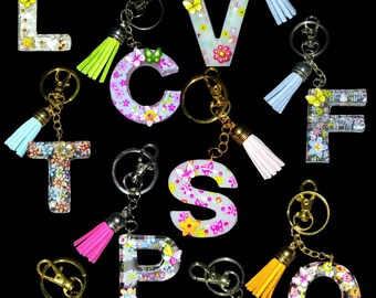 May include: A set of 10 colorful resin letter keychains with floral and butterfly designs. Each keychain features a different letter of the alphabet and a tassel.