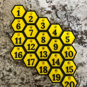 May include: A set of 20 yellow hexagonal numbered tags with black outlines and numbers. The tags are arranged in a honeycomb pattern.