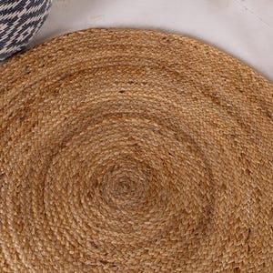 May include: A round, natural fiber rug with a woven texture. The rug is made of jute and has a light brown color.