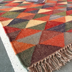 May include: A colourful geometric patterned rug with a fringe border. The rug is made of woven wool and features a variety of colours, including red, orange, yellow, green, blue, and brown.