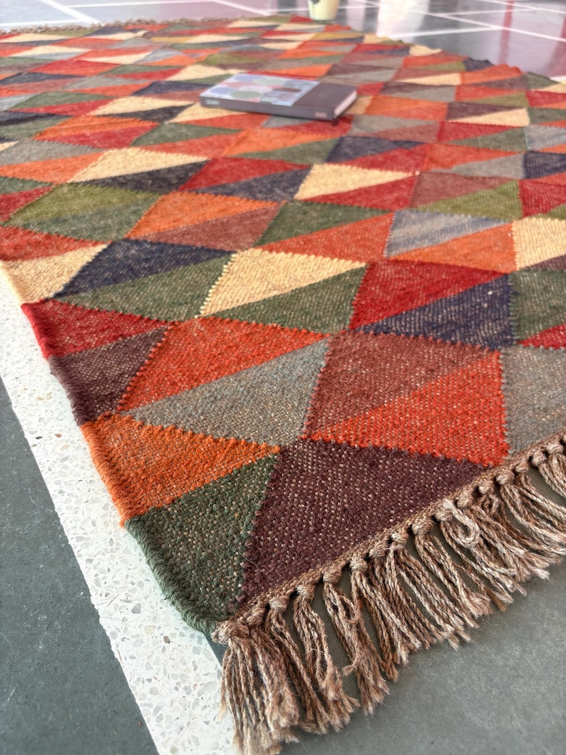 May include: A colourful geometric patterned rug with a fringe border. The rug is made of woven wool and features a variety of colours, including red, orange, yellow, green, blue, and brown.