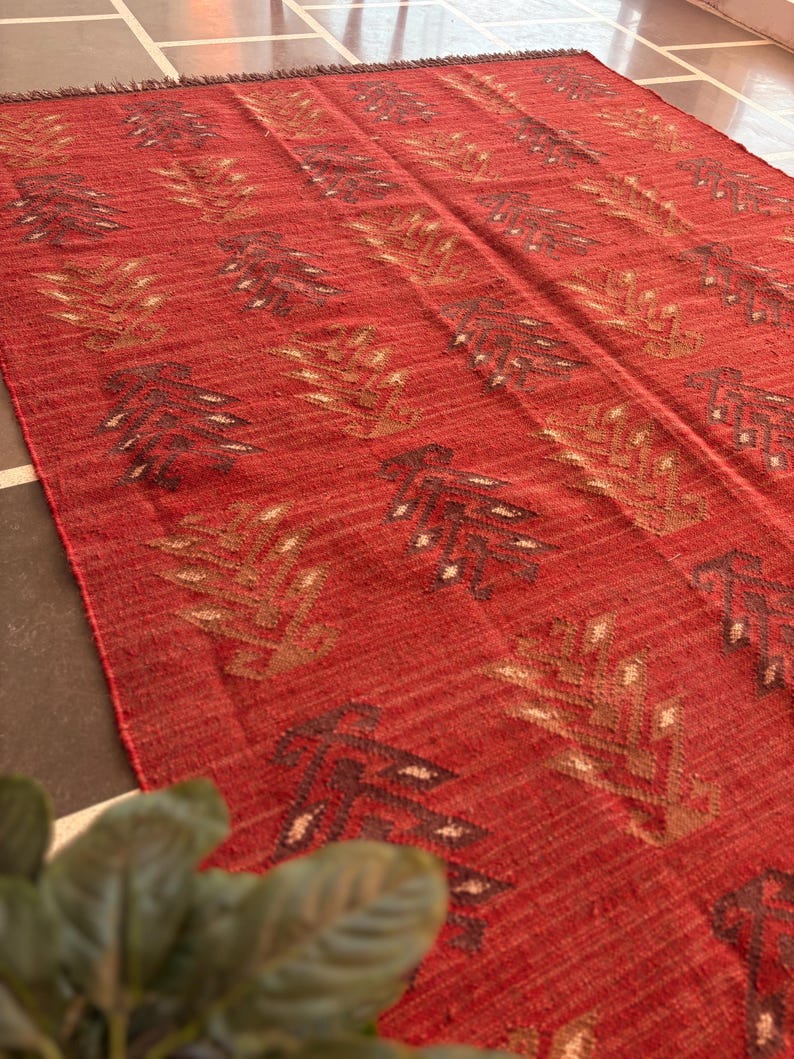 May include: Red, brown, and beige patterned rug with a woven texture. The rug has a geometric design with a repeating pattern of stylized leaves.
