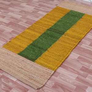Pode incluir: Um tapete retangular longo com um padr&atilde;o listrado. O tapete &eacute; feito de fibras naturais e tem um esquema de cores bege, amarelo e verde.