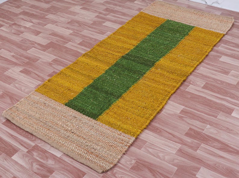 Pode incluir: Um tapete retangular longo com um padr&atilde;o listrado. O tapete &eacute; feito de fibras naturais e tem um esquema de cores bege, amarelo e verde.
