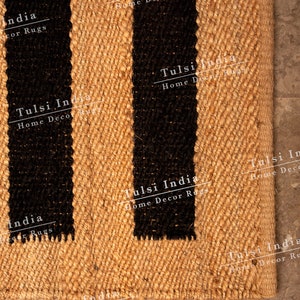 May include: A natural fibre rug with black stripes. The rug is made of jute and has a woven texture. The rug is labelled "Tulsi India Home Decor Rugs".