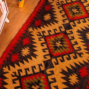 Puede incluir: Primer plano de una alfombra tejida colorida con un patr&oacute;n geom&eacute;trico en tonos rojos, negros, amarillos y verdes. La alfombra tiene un dise&ntilde;o tradicional con detalles intrincados.