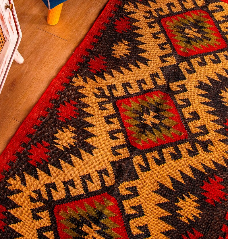 Puede incluir: Primer plano de una alfombra tejida colorida con un patr&oacute;n geom&eacute;trico en tonos rojos, negros, amarillos y verdes. La alfombra tiene un dise&ntilde;o tradicional con detalles intrincados.