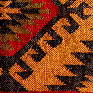 Puede incluir: Primer plano de una alfombra tejida con un patr&oacute;n geom&eacute;trico en tonos rojos, naranjas, negros y verdes.
