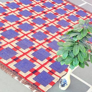 May include: A blue, red, and beige geometric patterned rug with fringe. The rug is made of woven wool and has a contemporary design.