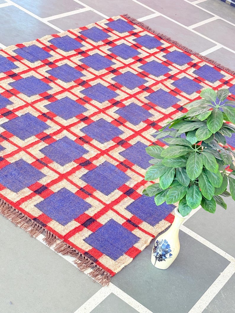 May include: A blue, red, and beige geometric patterned rug with fringe. The rug is made of woven wool and has a contemporary design.
