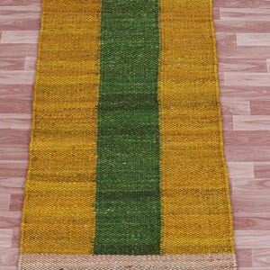 Pode incluir: Um tapete retangular de juta com um padr&atilde;o listrado. O tapete tem uma borda bege, uma faixa amarela, uma faixa verde e outra faixa amarela.