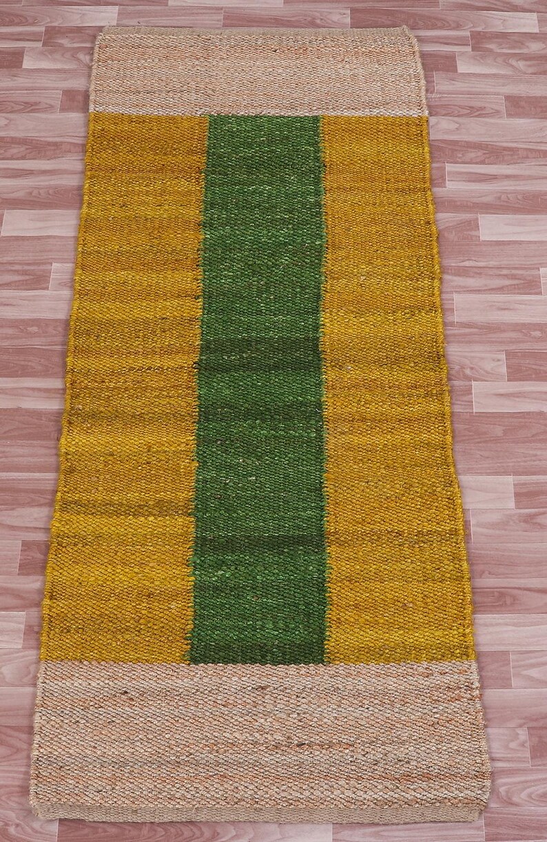 Pode incluir: Um tapete retangular de juta com um padr&atilde;o listrado. O tapete tem uma borda bege, uma faixa amarela, uma faixa verde e outra faixa amarela.
