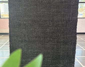 May include: A black woven rug with a jute border. The rug has a textured surface and is made of natural fibers.